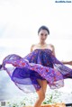 A woman in a purple dress is posing by the water.