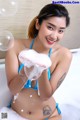 A woman in a blue bikini sitting in a bathtub with soap bubbles.