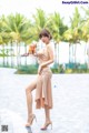 A woman in a beige dress posing by a pool.