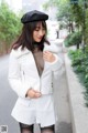 A woman in a white jacket and black hat is walking down the street.