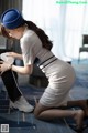 A woman in a white dress and a blue hat crouching on the floor.