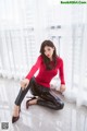 A woman in a red shirt and black pants sitting on the floor.