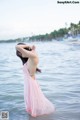 A woman in a pink dress standing in the water.