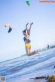 A woman in a bikini jumping in the air with a kite.