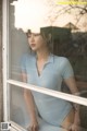 A woman in a blue bodysuit leaning against a window.