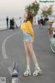 A woman in a yellow top and denim shorts standing on the street.