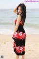 A woman in a red and black dress standing on a beach.