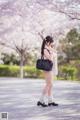 A woman standing in front of a tree with a black bag.