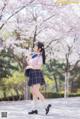 A woman in a school uniform is walking in front of cherry blossoms.