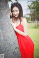 A woman in a red dress leaning against a palm tree.