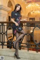 A woman in a black dress and high heels posing on a balcony.