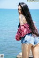 A woman in a red and white plaid shirt and denim shorts posing by the water.