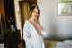 A woman in a white robe standing in a bedroom.