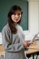 A woman standing in front of a blackboard holding a piece of paper.