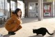 A woman crouching down next to a black cat.