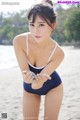 A woman in a blue bathing suit holding a shell on the beach.