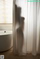 A woman standing in front of a white curtain in a bathroom.