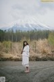 A woman standing in a field with a mountain in the background.