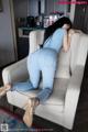 A woman in a blue top and jeans sitting on a white chair.