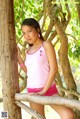 A young woman leaning against a tree in a pink tank top.