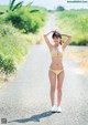 A woman in a yellow bikini standing on a dirt road.