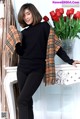 A woman in a black turtle neck sweater and plaid scarf posing for a picture.