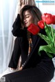 A woman sitting on a window sill next to a vase of red tulips.