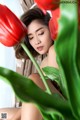 A woman sitting on a bed next to a bunch of red tulips.