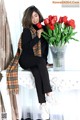 A woman sitting on a table with a vase of red tulips.