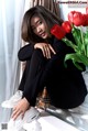 A woman sitting on a window sill next to a vase of red tulips.