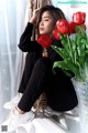 A woman sitting on a window sill next to a vase of red tulips.