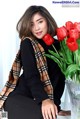 A woman sitting next to a vase of red tulips.