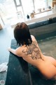 A woman with a tattoo on her back sitting in a bathtub.