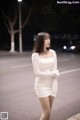 A woman in a white dress standing on the street at night.