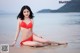 A woman in a red bikini sitting on the beach.