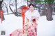 A woman in a kimono standing in the snow holding an umbrella.