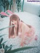 A woman in a pink bunny costume crouching on a bed of white pebbles.