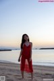 A woman in a red dress standing on a beach.