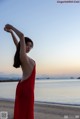 A woman in a red dress standing on a beach.