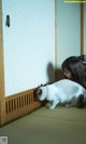 A woman is petting a white cat on the floor.