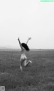 A naked woman standing in a field with her arms outstretched.