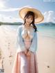 A woman in a pink dress and a straw hat on a beach.