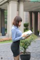 A woman in a blue shirt and black skirt holding a tablet.