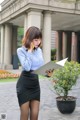 A woman in a blue shirt and black skirt talking on a cell phone.