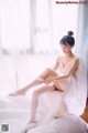 A woman sitting on top of a bed in a white dress.