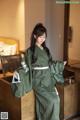 A woman in a green kimono standing in a hotel room.