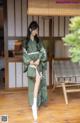 A woman in a green kimono standing on a wooden floor.