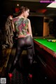 A woman with a tattoo on her back standing next to a pool table.