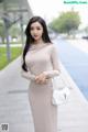 A woman in a beige dress holding a white purse.