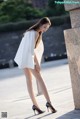 A woman in a white dress and black shoes leaning against a wall.